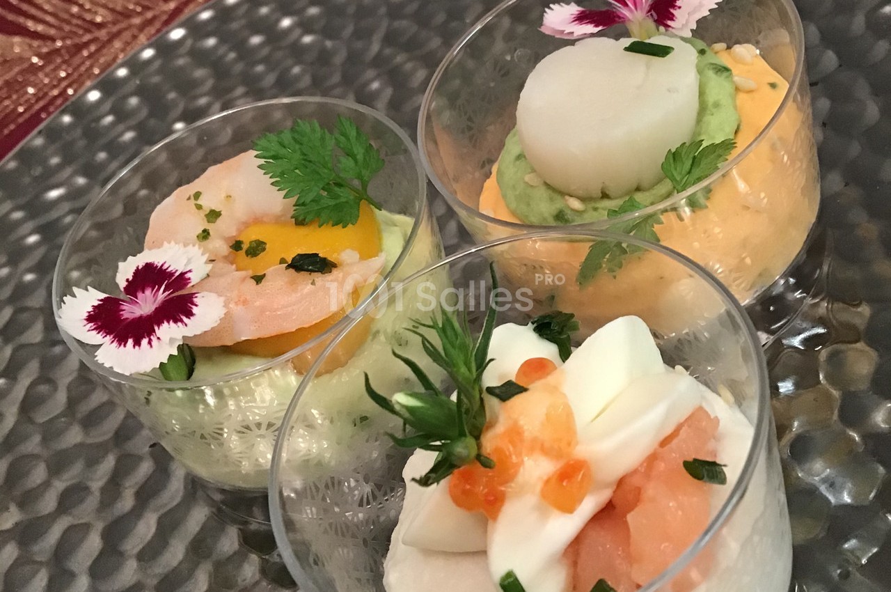 Trois verrines garnies de crevettes, saumon, purées colorées et décorations florales sur un plateau métallique.