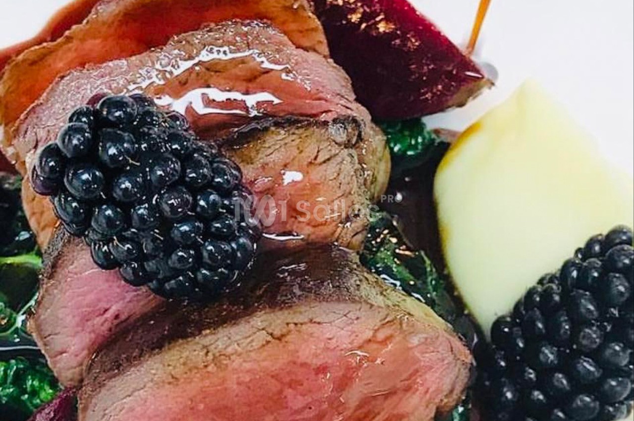 Plat de viande rosée garnie de mûres, accompagnée de purée et légumes, nappée d'une sauce brillante.