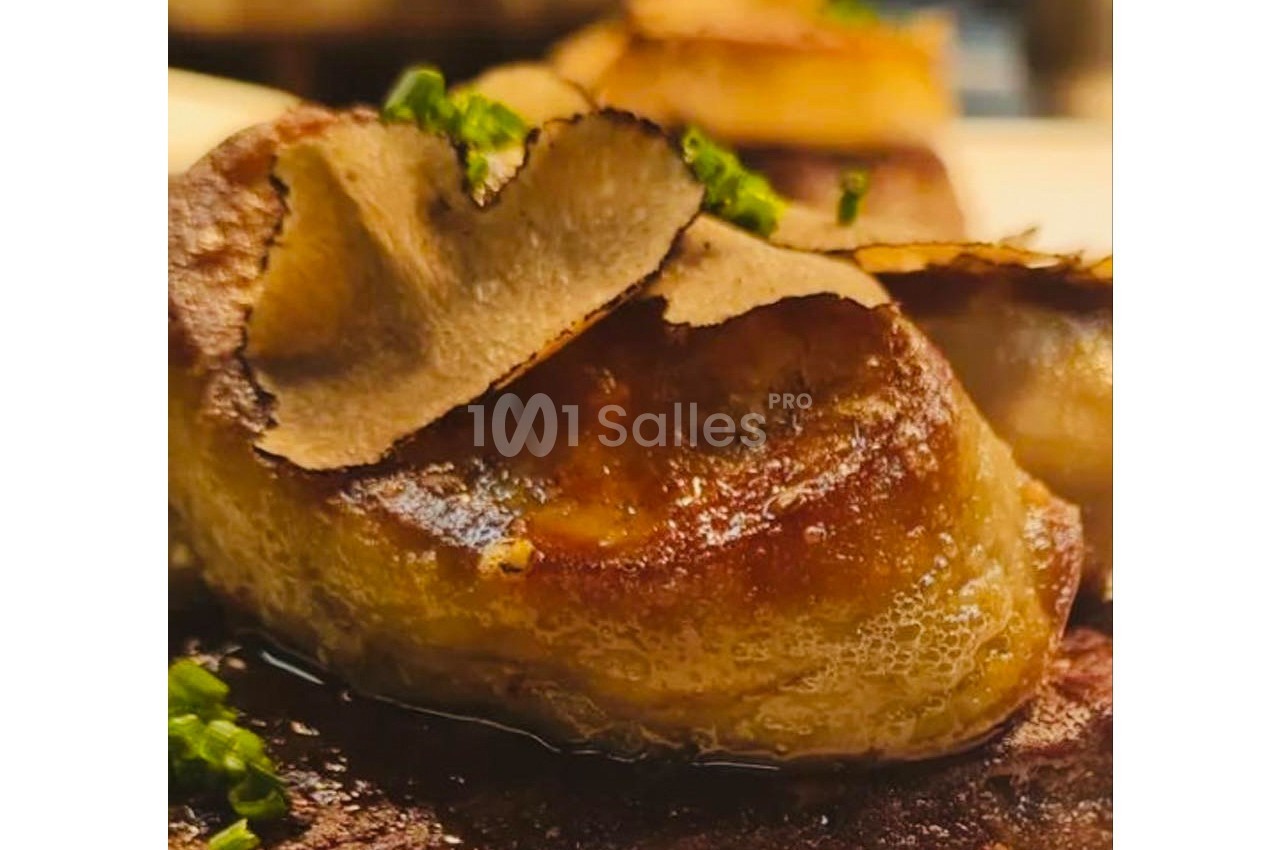Tranche de foie gras poêlé garnie de lamelles de truffe, servie avec une touche de ciboulette.