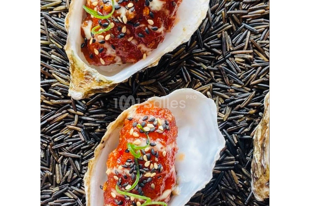 Huîtres garnies de tartare épicé, graines de sésame et oignons verts, présentées sur un lit de riz sauvage.