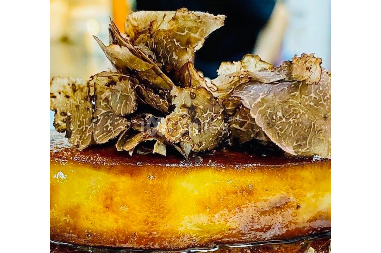 Gâteau doré garni de fines tranches de truffe noire, présenté dans un environnement lumineux.