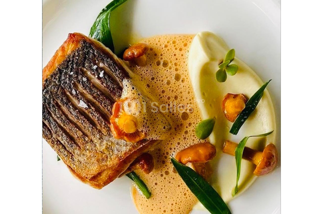 Filet de poisson grillé avec purée onctueuse, girolles, herbes fraîches et sauce mousseuse sur une assiette blanche.