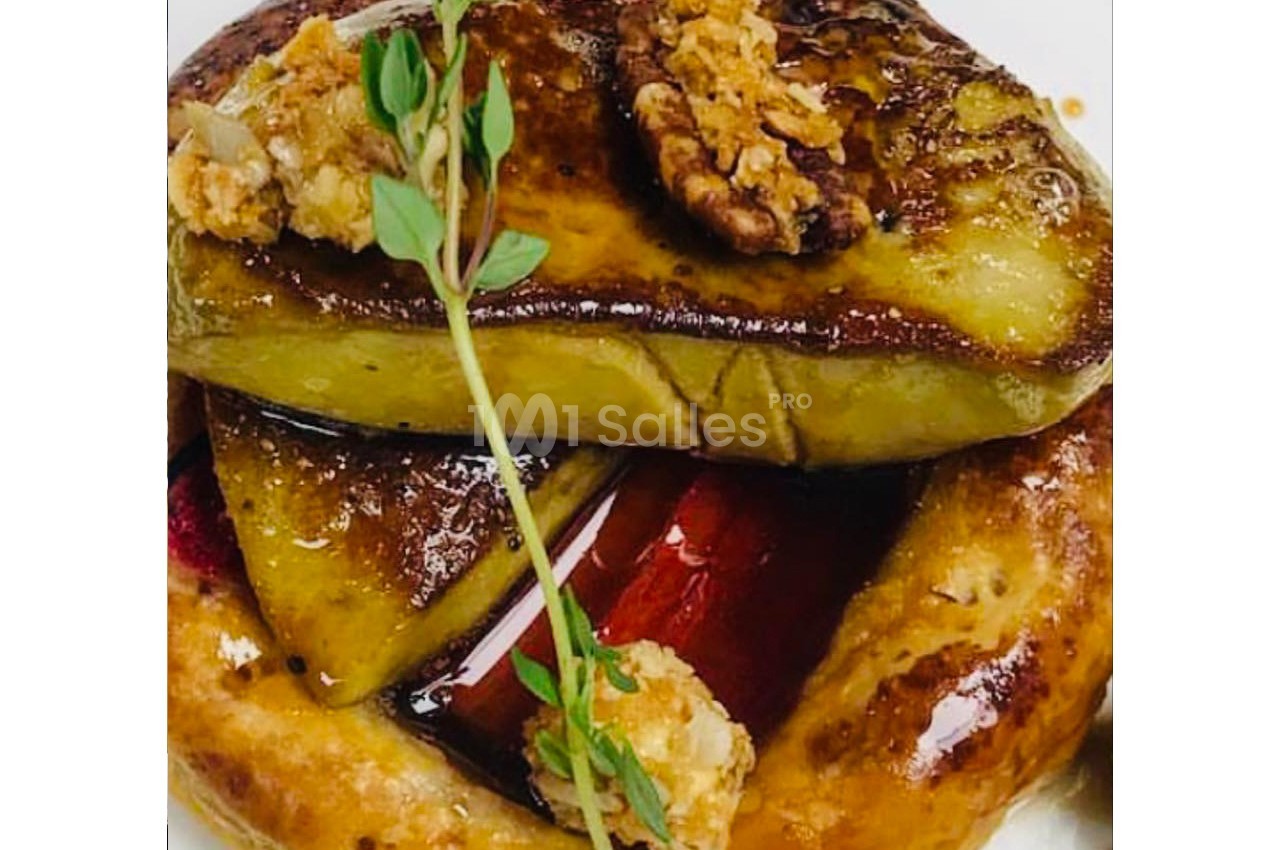 Tartelette garnie de foie gras poêlé, noix caramélisées et branche de thym, servie sur une assiette blanche.