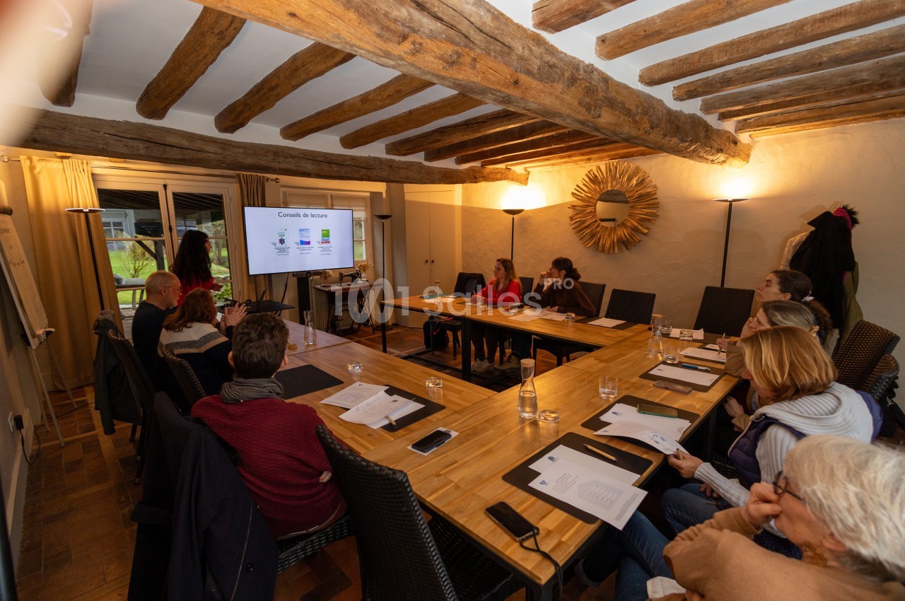 Un groupe de personnes assises autour d'une table en bois suit une présentation projetée sur un écran dans une salle.