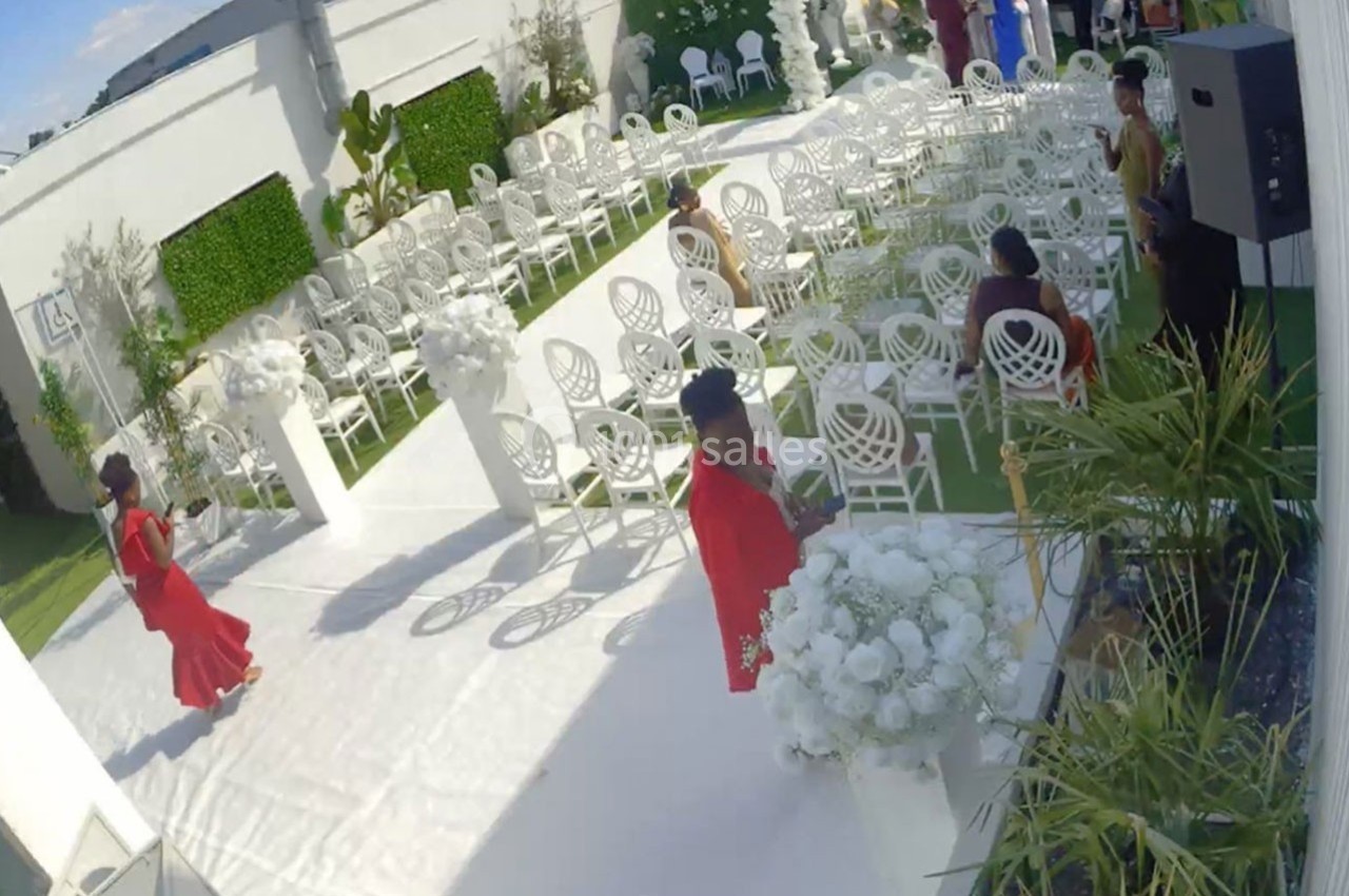 Chaises blanches alignées pour une cérémonie en extérieur, avec des décorations florales et quelques invités présents.