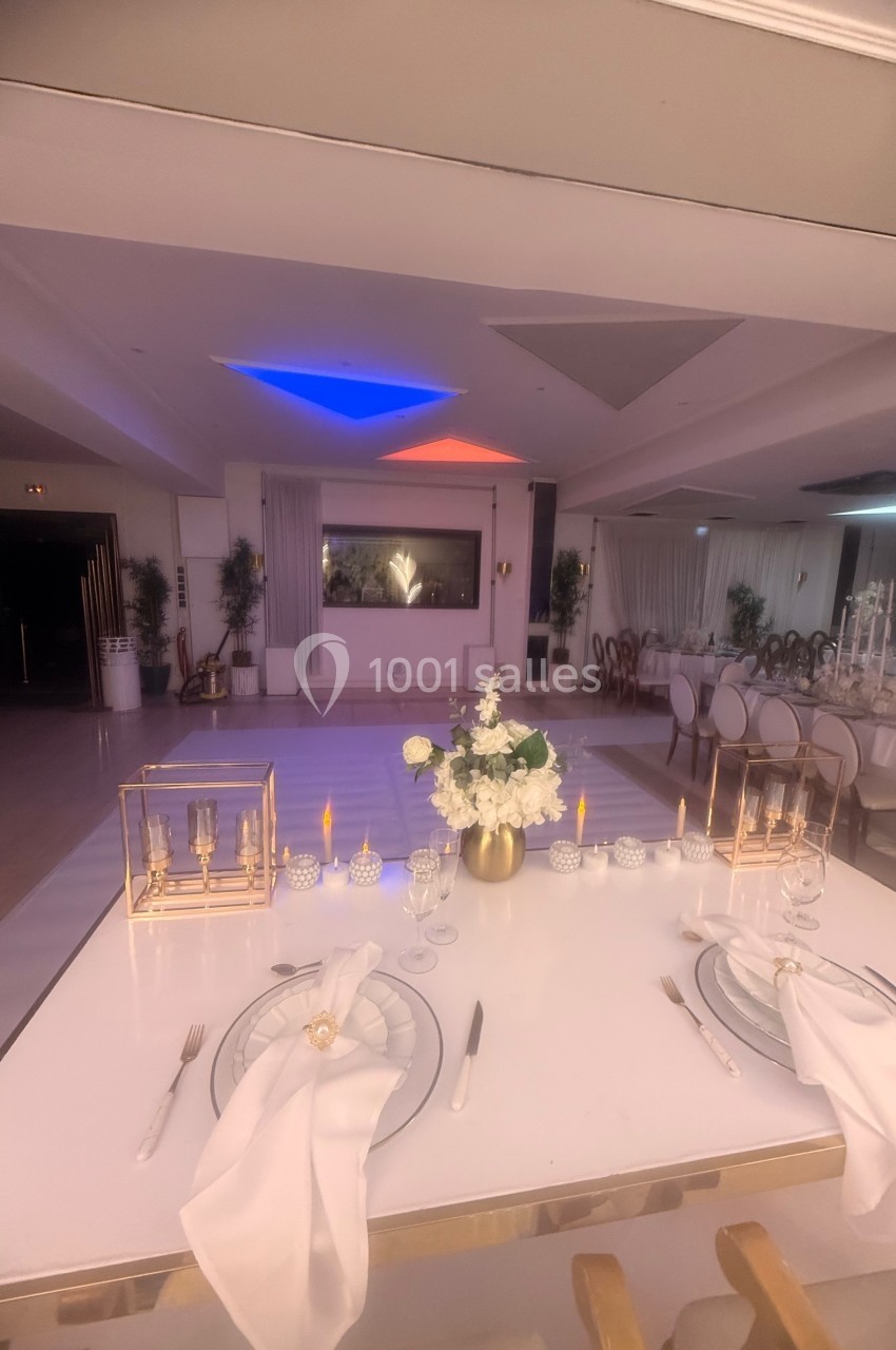 Table élégamment dressée avec des assiettes, serviettes et bougies, dans une salle de réception décorée et éclairée.