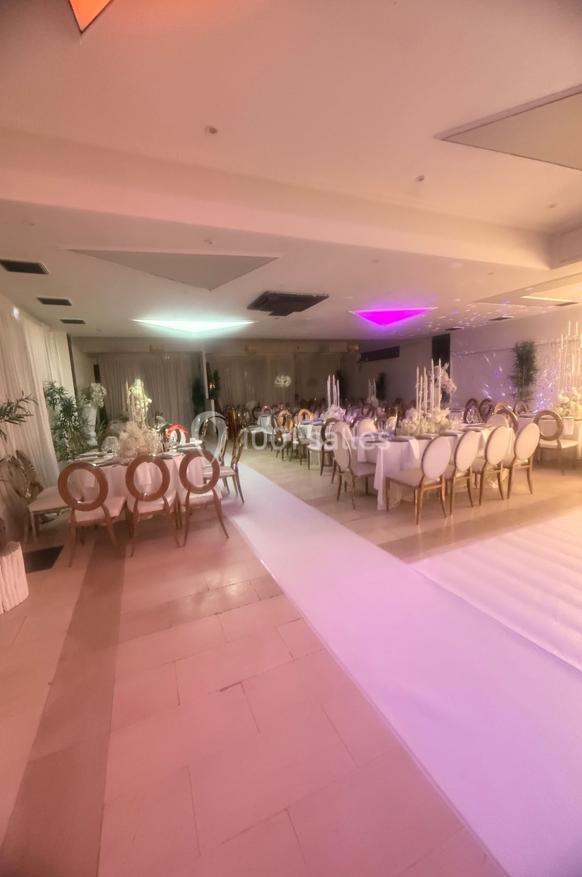 Salle de réception élégante avec tables décorées, chaises blanches et éclairage tamisé dans une ambiance festive.