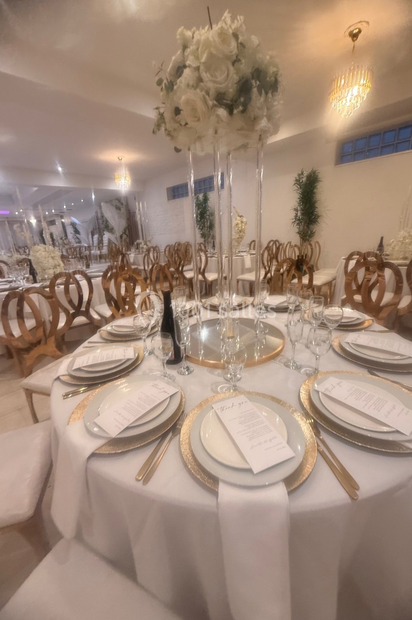 Table élégamment dressée avec vaisselle raffinée, menus et centre de table floral dans une salle de réception lumineuse.