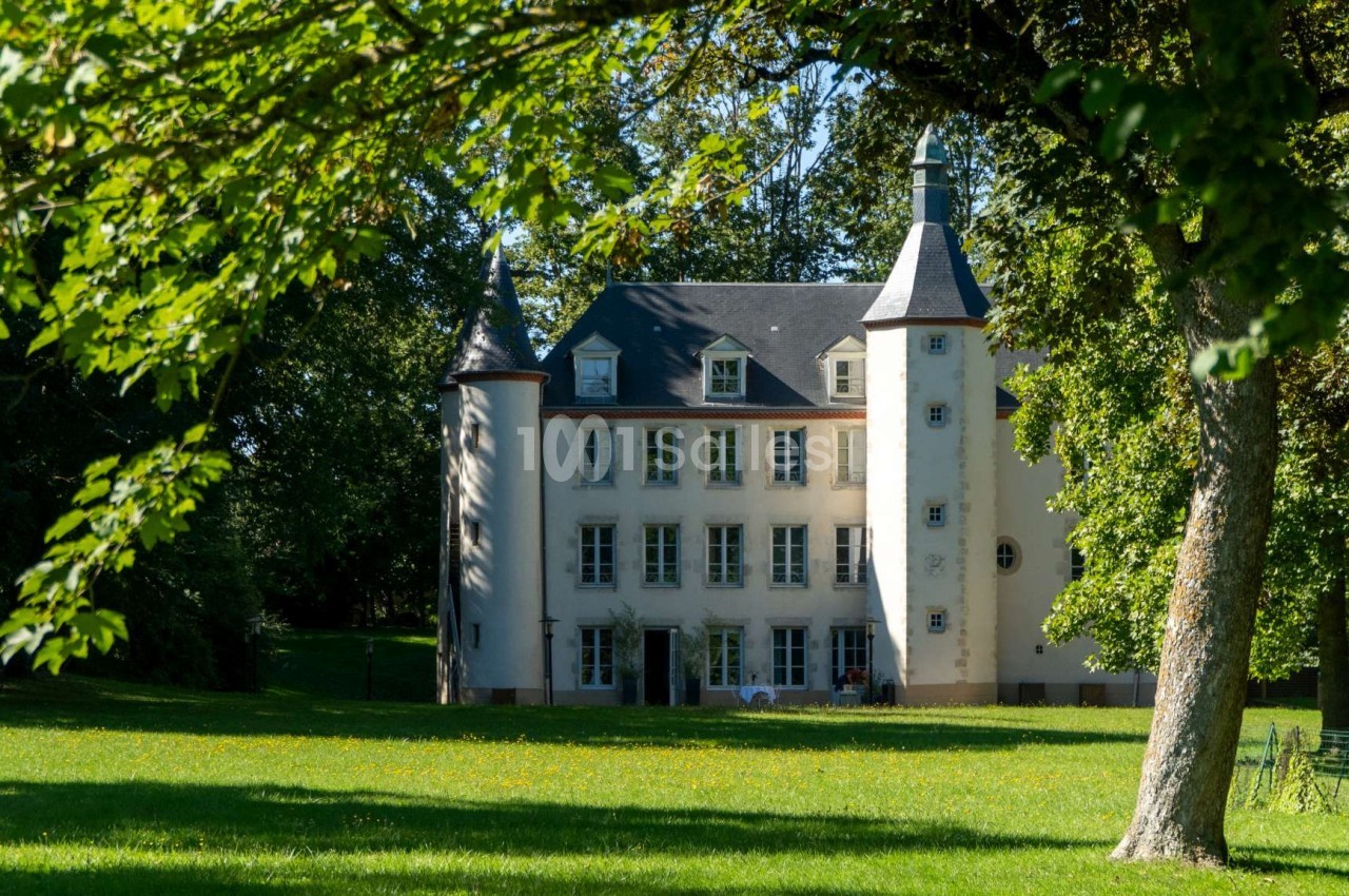 Façade d'un petit château blanc entouré d'arbres et d'une pelouse verdoyante sous un ciel dégagé.