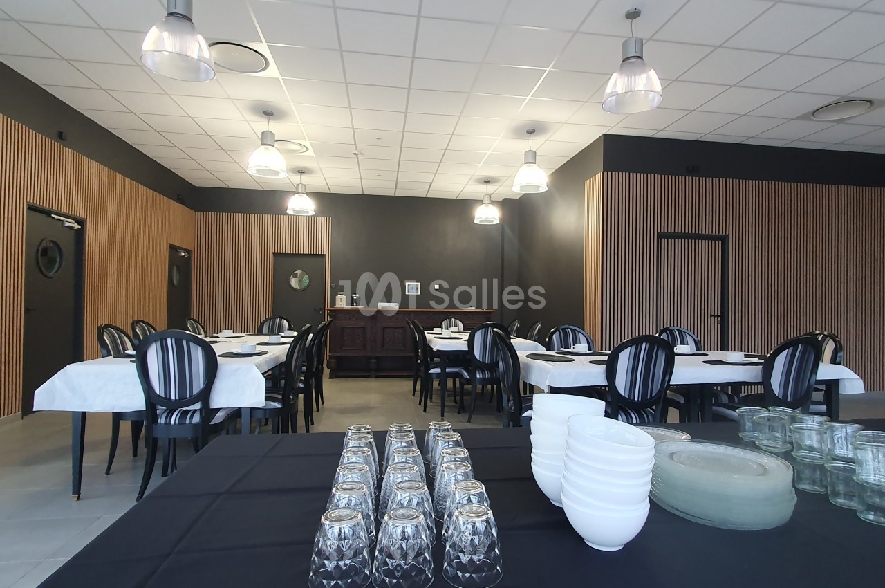 Salle de réception avec tables dressées, chaises noires, murs sombres et un buffet en arrière-plan.