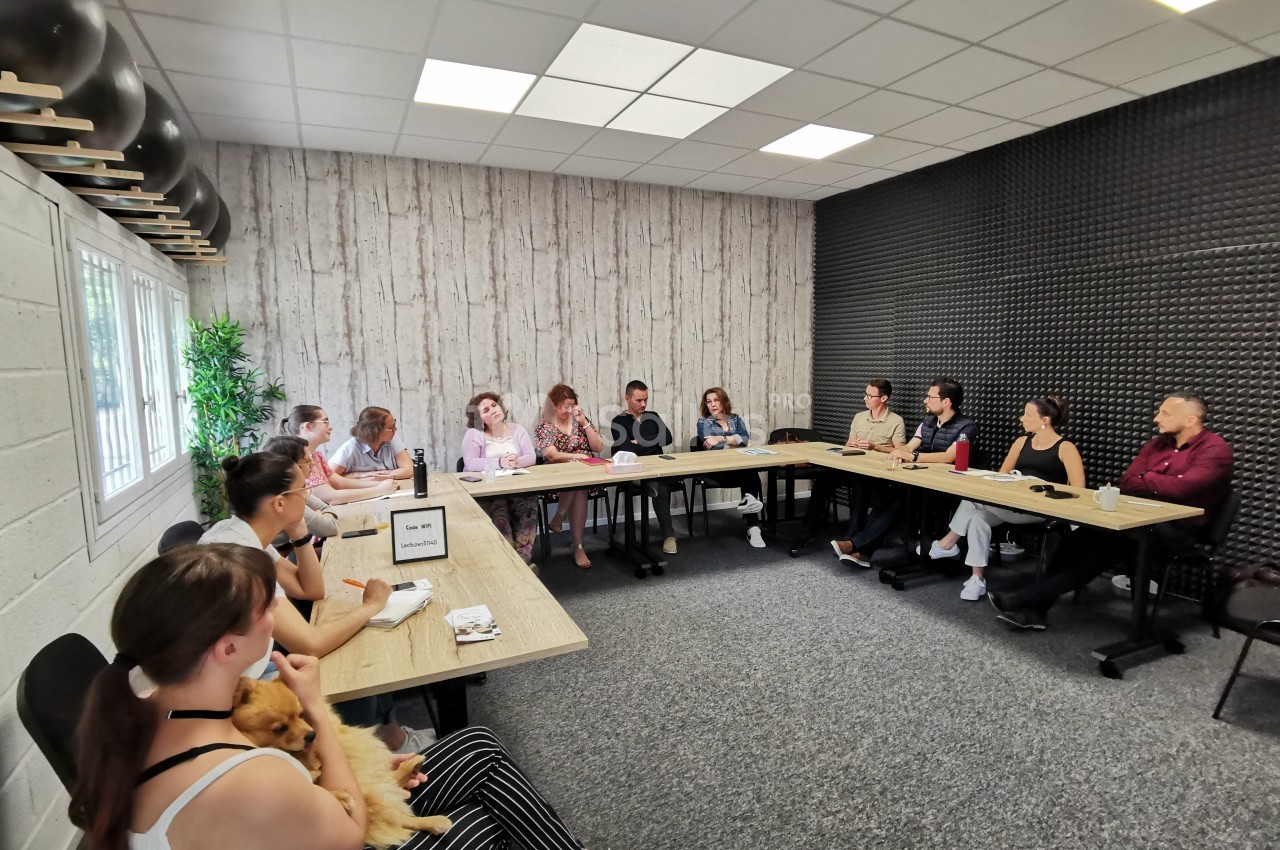 Un groupe de personnes assises autour de tables en réunion dans une salle lumineuse avec un mur en bois et un autre…