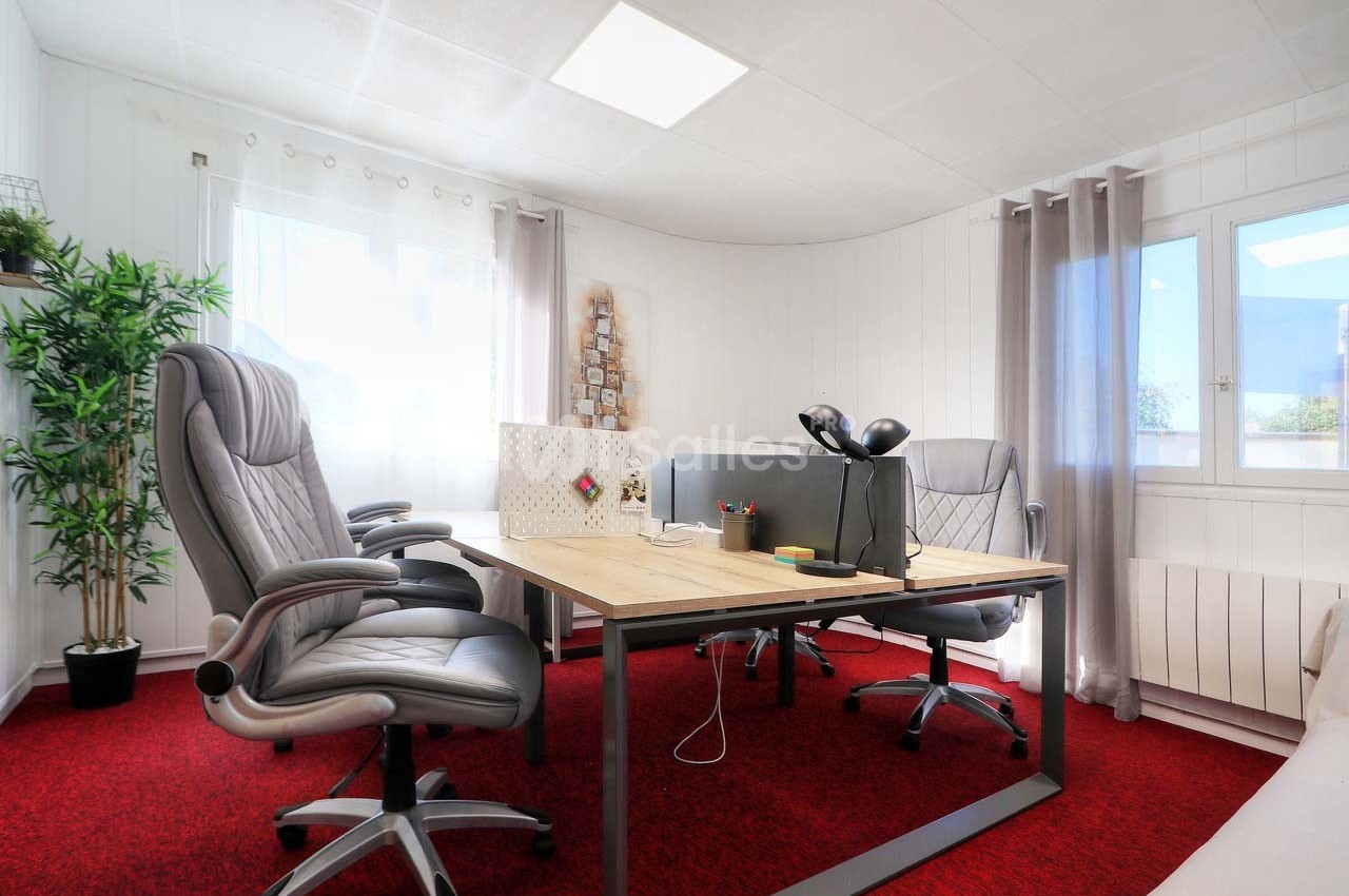 Bureau lumineux avec deux fauteuils gris, une table en bois, un séparateur de bureau et une fenêtre donnant sur l'extérieur.