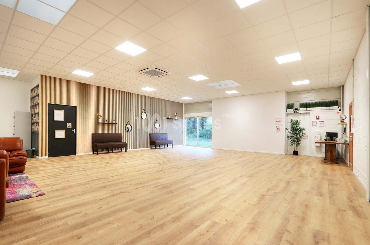 Salle spacieuse avec parquet clair, murs décorés, canapés, étagères et grande baie vitrée donnant sur l'extérieur.