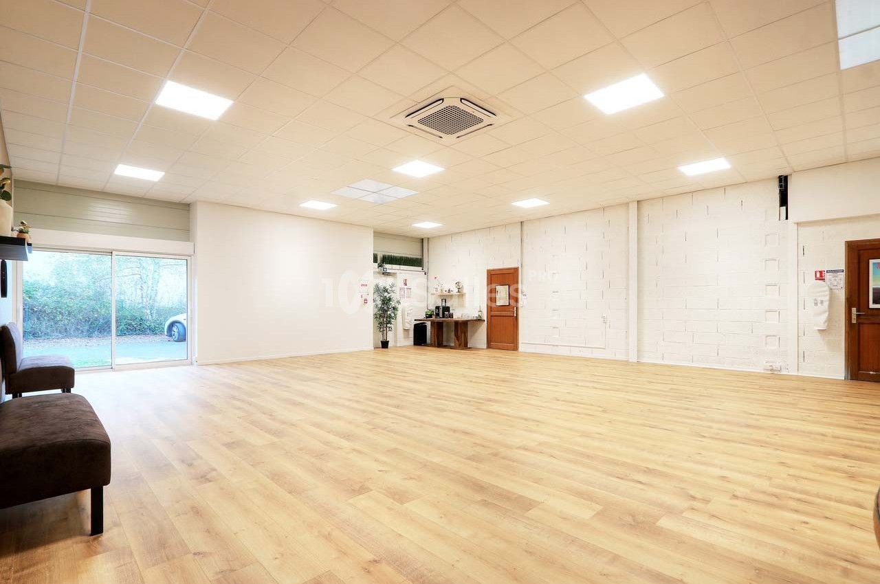Salle spacieuse avec parquet clair, murs blancs, éclairage au plafond et une baie vitrée donnant sur l'extérieur.
