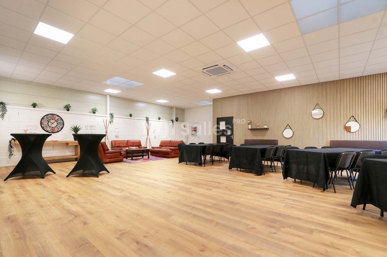 Salle lumineuse avec parquet, tables noires, fauteuils en cuir, décorations murales et plantes suspendues.