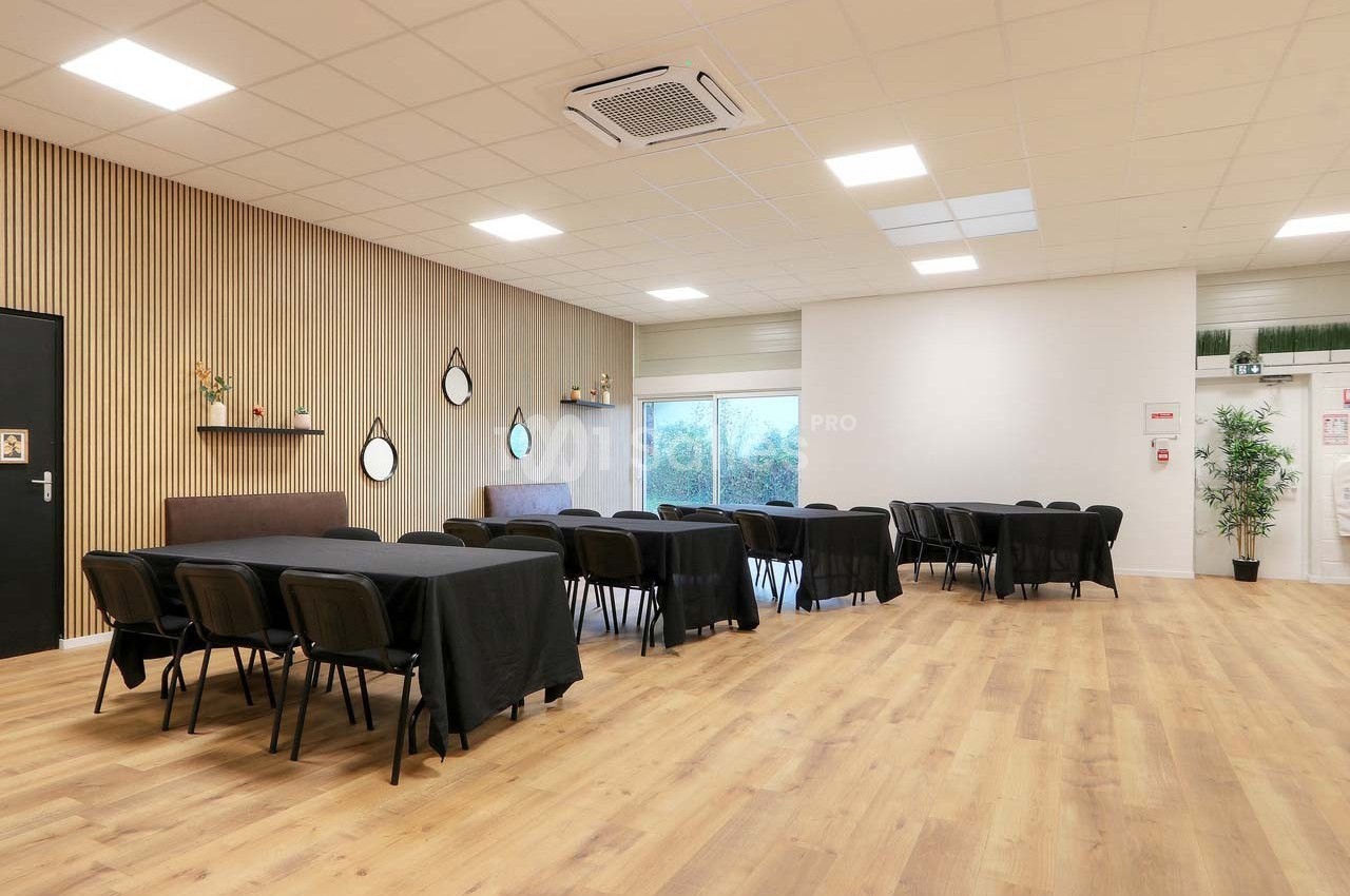 Salle lumineuse avec parquet, tables noires alignées, chaises, murs clairs et décorations murales modernes.