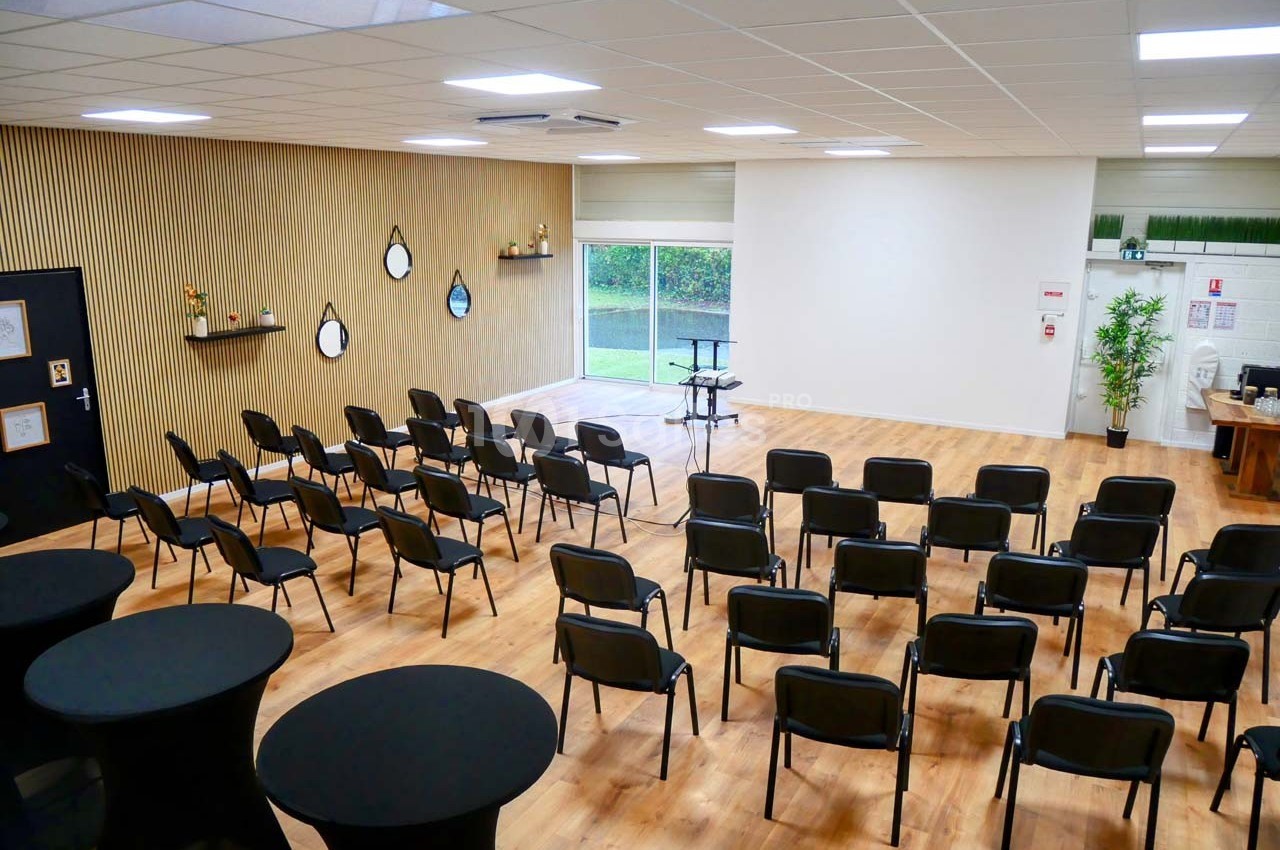 Salle de conférence lumineuse avec chaises alignées, tables hautes noires et décorations murales modernes.