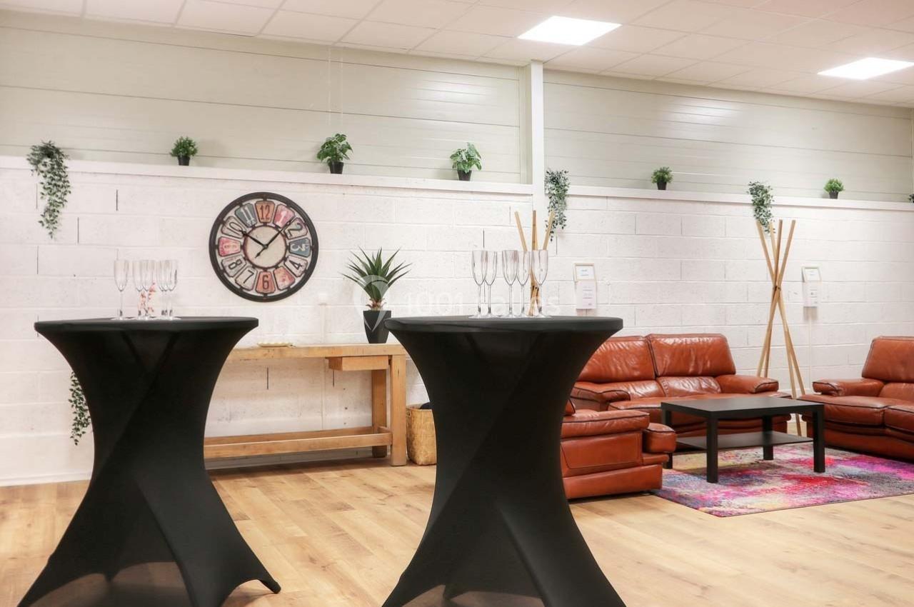Salle aménagée avec des canapés en cuir, tables hautes avec verres, décorations murales et plantes suspendues.