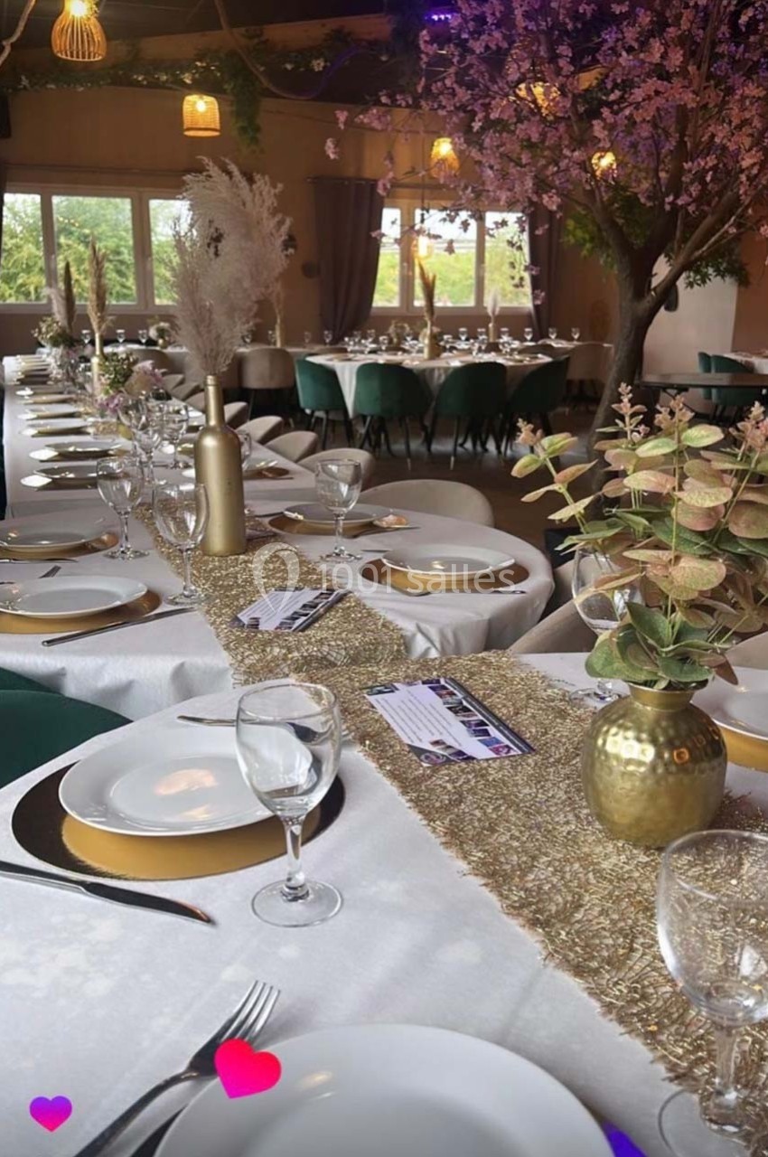 Table décorée pour un événement avec nappes blanches, vaisselle élégante, chemins de table dorés et arrangements floraux.