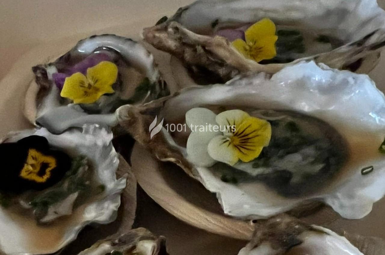 Huîtres ouvertes garnies de fleurs comestibles colorées et de fines herbes, présentées sur un plateau.