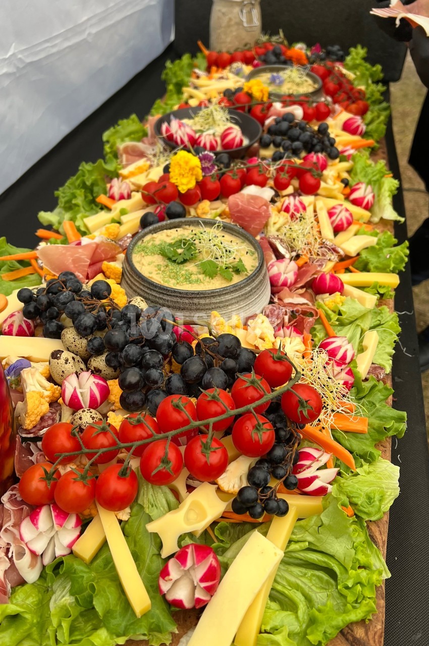 Plateau coloré de charcuteries, fromages, légumes frais et fruits, disposés autour d'une sauce au centre.