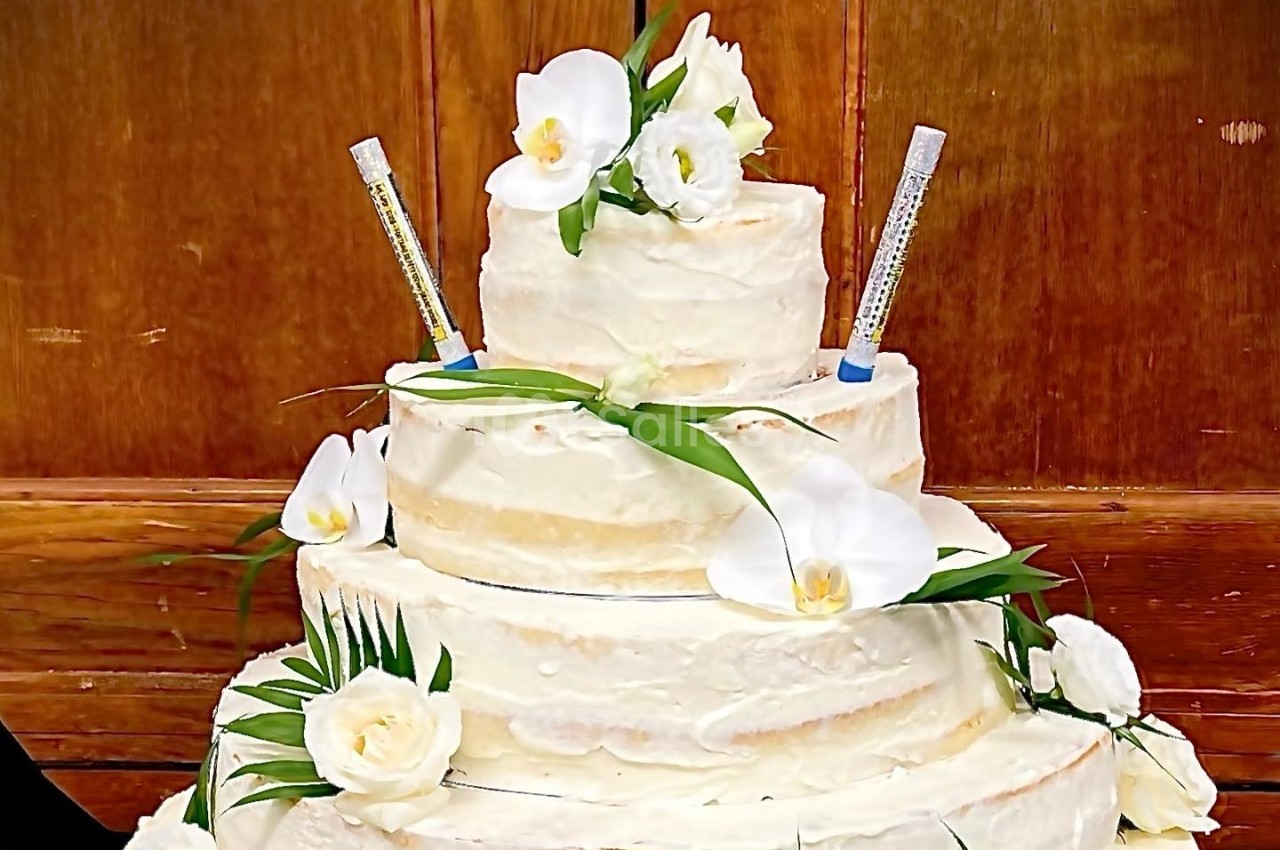 Gâteau de mariage à trois étages décoré de fleurs blanches et de seringues en guise d'éléments décoratifs.