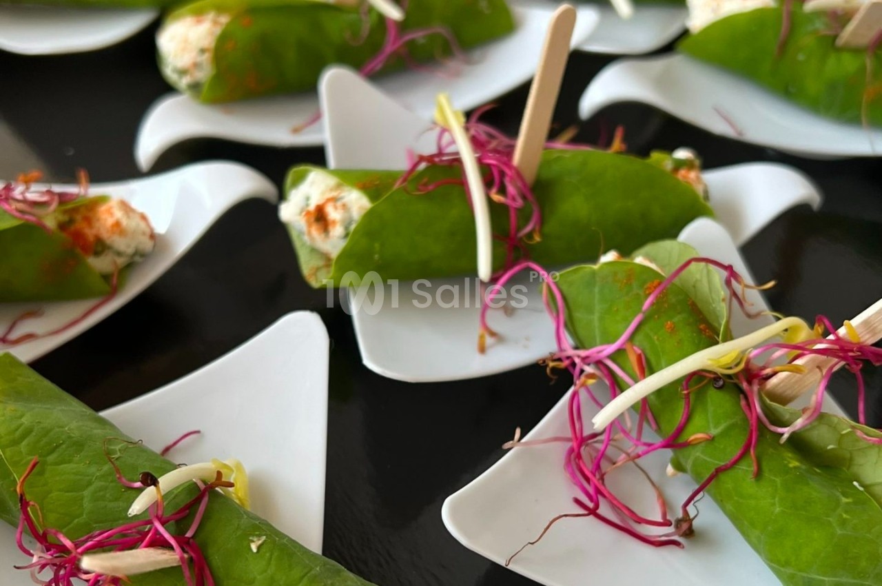 Rouleaux de feuilles vertes garnis de fromage frais, décorés de pousses roses et présentés sur des assiettes individuelles…