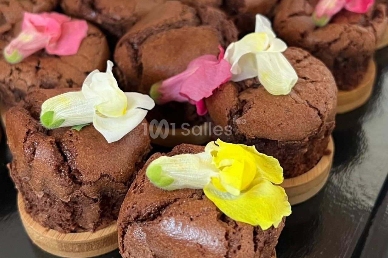 Petits gâteaux au chocolat décorés de fleurs comestibles colorées, présentés sur des supports en bois.