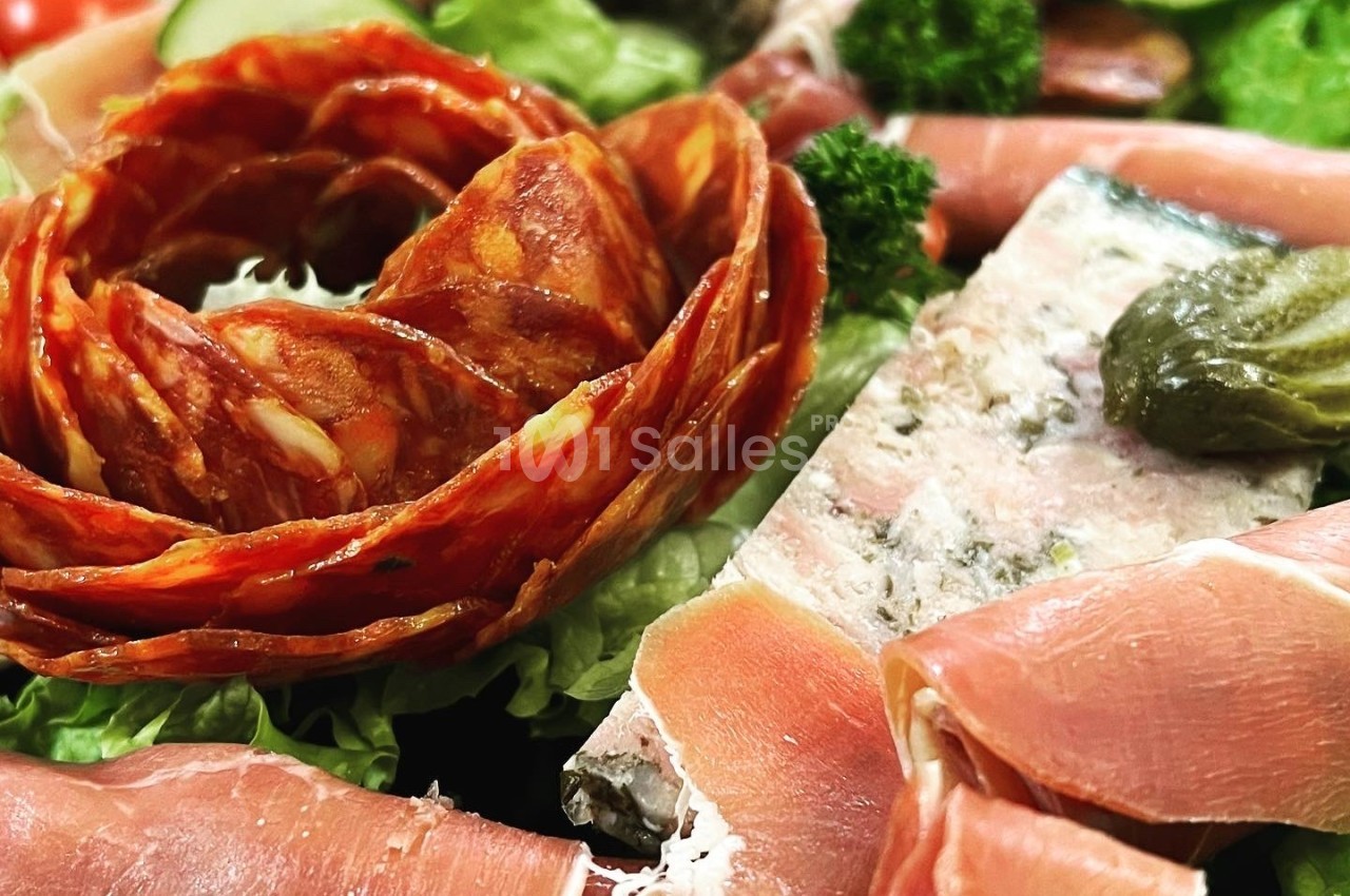 Plateau de charcuterie avec chiffonnade de jambon, rondelles de chorizo en forme de fleur et terrine garnie de cornichons.