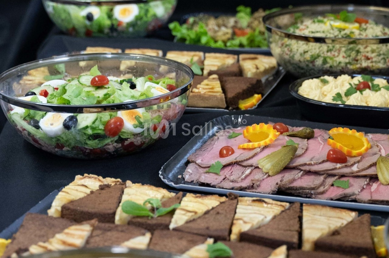 Buffet composé de salades, tranches de rôti garnies, parts de gâteaux et autres plats variés sur une nappe noire.