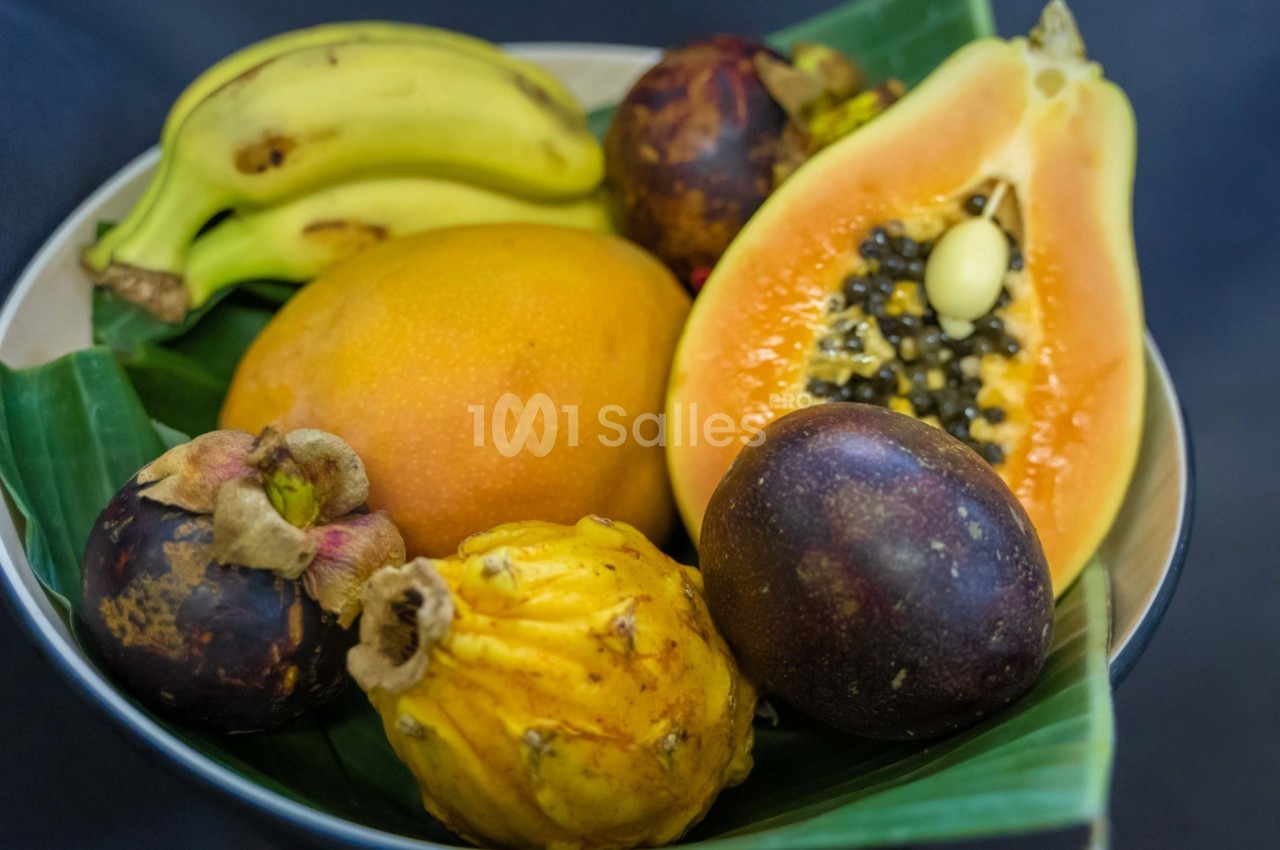 Assortiment de fruits tropicaux comprenant bananes, papaye, mangoustan, fruit de la passion et pitaya sur une feuille verte.