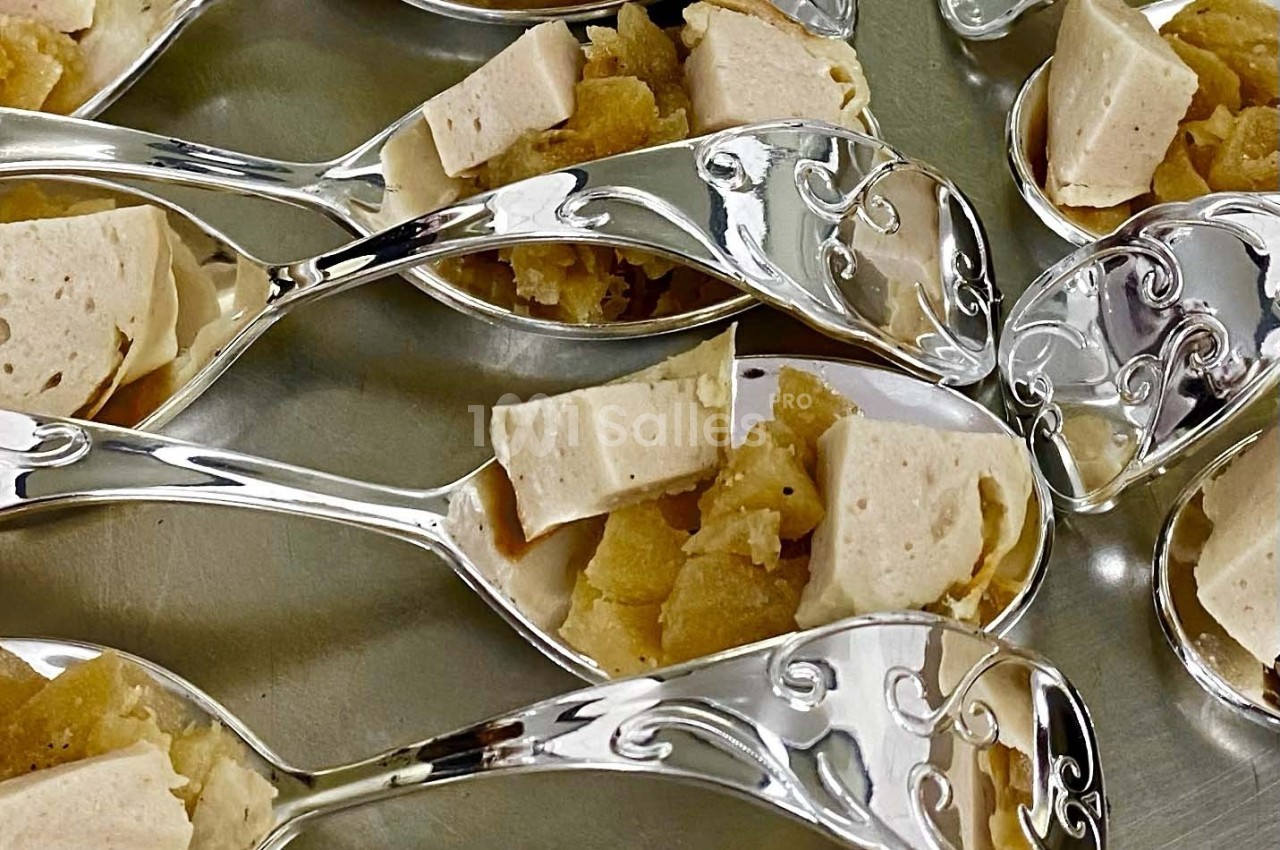 Cuillères en métal décoré contenant des morceaux de tofu et une garniture dorée sur une surface argentée.