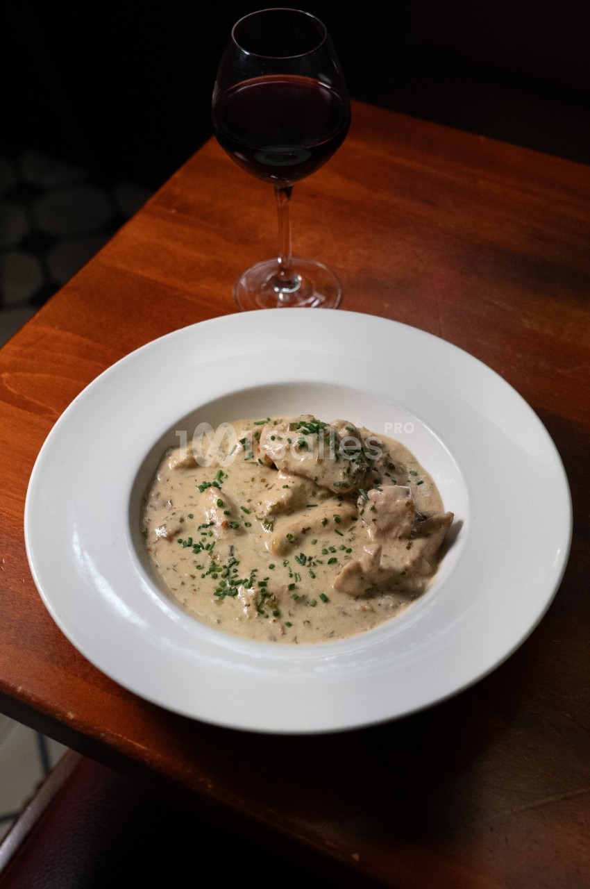 Assiette de blanquette de veau servie avec une sauce crémeuse, garnie de ciboulette, accompagnée d'un verre de vin rouge.