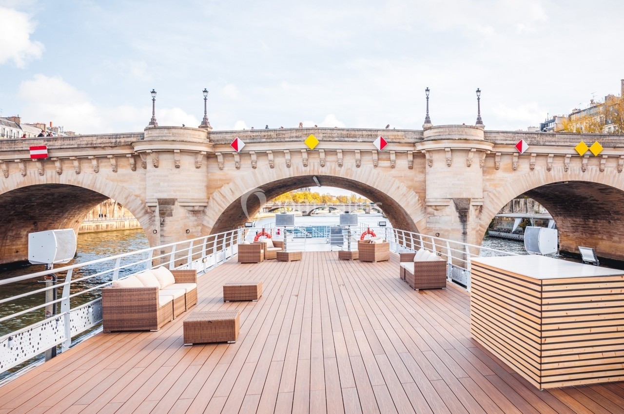 Pont en pierre traversant une rivière, vu depuis le ponton en bois d'un bateau avec mobilier de salon extérieur.