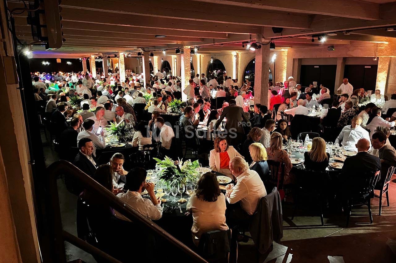 Salle remplie de convives assis à des tables rondes, éclairée par une lumière chaleureuse lors d'un événement.