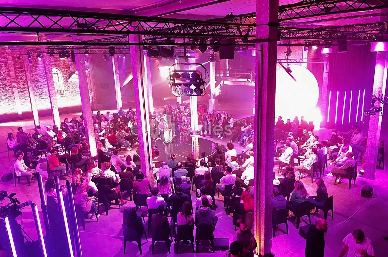 Vue d'une salle de conférence avec un public assis en cercle, éclairée par des lumières violettes et roses.