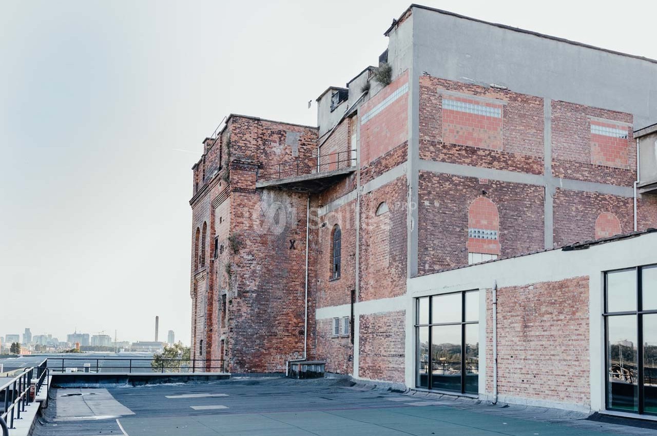 Bâtiment en briques rouges avec des fenêtres modernes, situé sur un toit-terrasse avec vue sur une ville à l'arrière-plan.