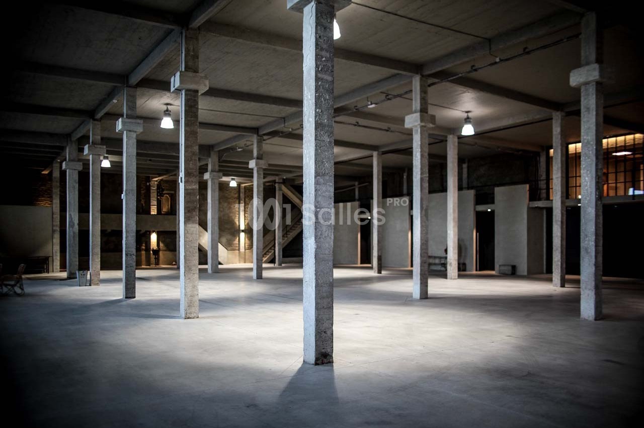 Intérieur d'un vaste entrepôt vide avec des colonnes en béton et un éclairage suspendu.