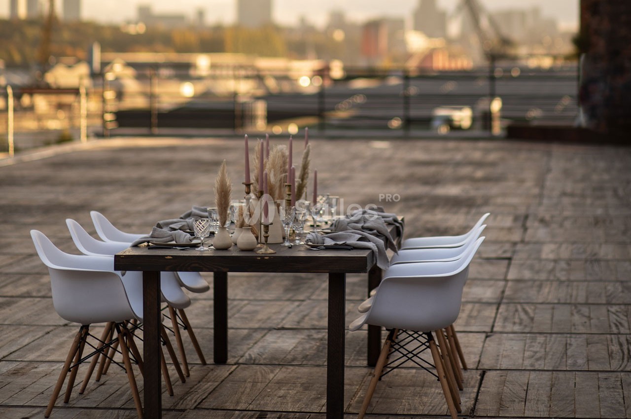Table dressée avec des bougies et des décorations sur une terrasse en bois, vue sur une ville en arrière-plan.