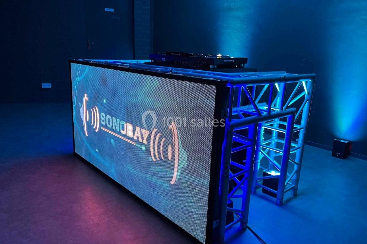 Console DJ éclairée avec écran LED affichant le logo ’Sonobay’, entourée de lumières bleues dans une salle sombre.