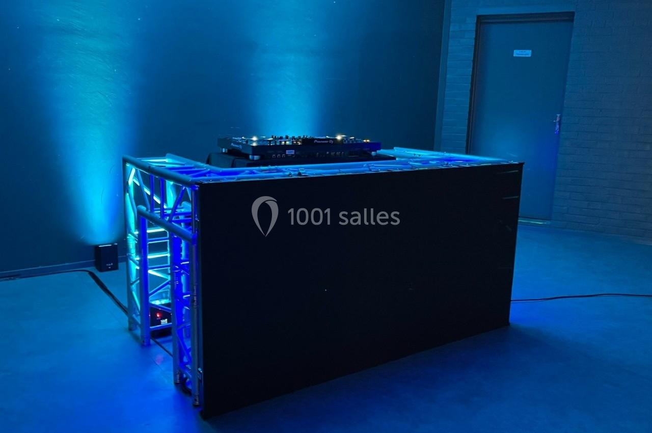 Table de mixage éclairée par des lumières bleues dans une salle sombre avec une porte grise en arrière-plan.