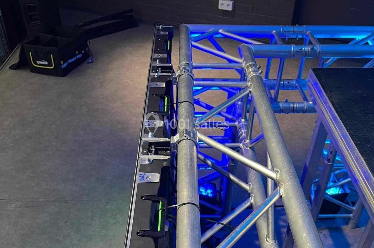 Structure métallique de scène avec éclairage bleu et équipements techniques en arrière-plan.