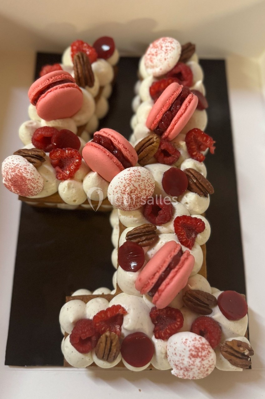 Gâteau en forme de chiffre décoré de macarons roses, framboises, noix de pécan et crème blanche.