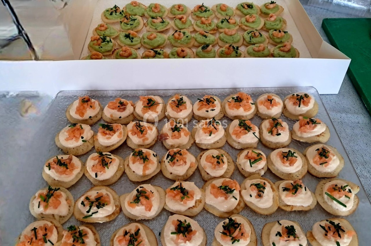 Plateau de canapés garnis de crème, saumon et herbes fraîches, avec un second plateau de bouchées vertes en arrière-plan.
