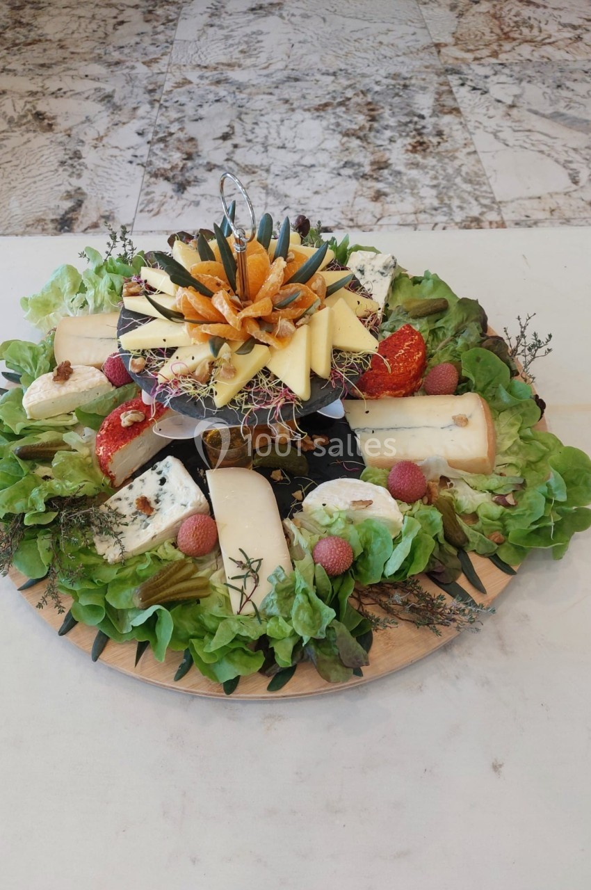 Plateau de fromages variés avec fruits, légumes et décorations sur un lit de salade, présenté sur une table.