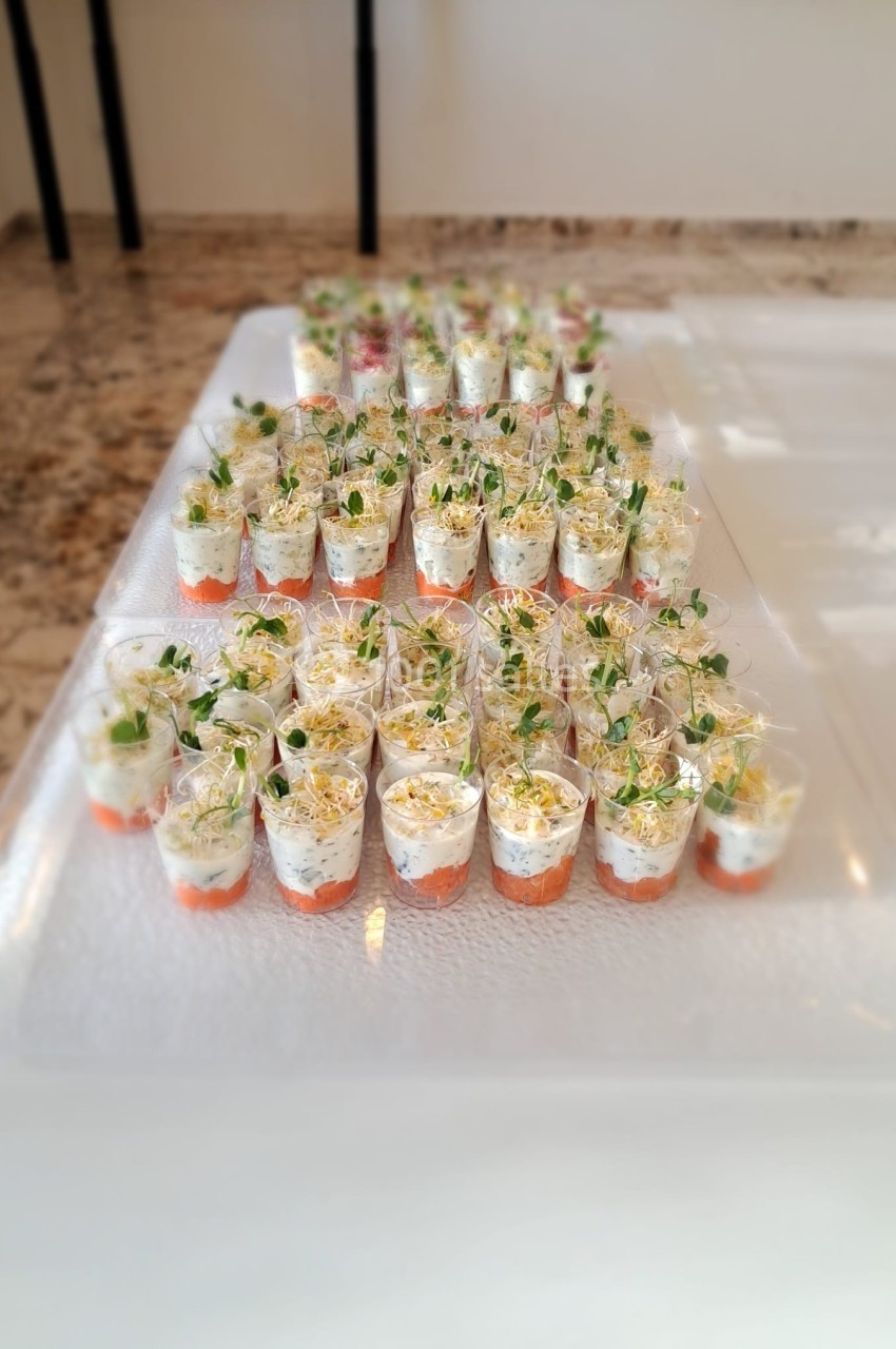 Verrines disposées en rangées sur une table, contenant des couches de saumon, crème et pousses fraîches.