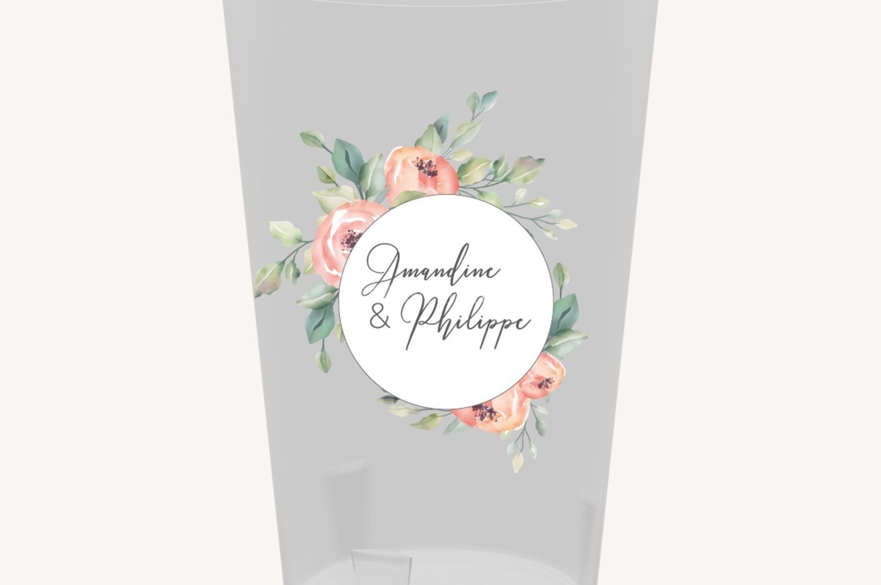 Verre transparent décoré d'un motif floral et d'un cercle blanc contenant les prénoms ’Amandine & Philippe’.