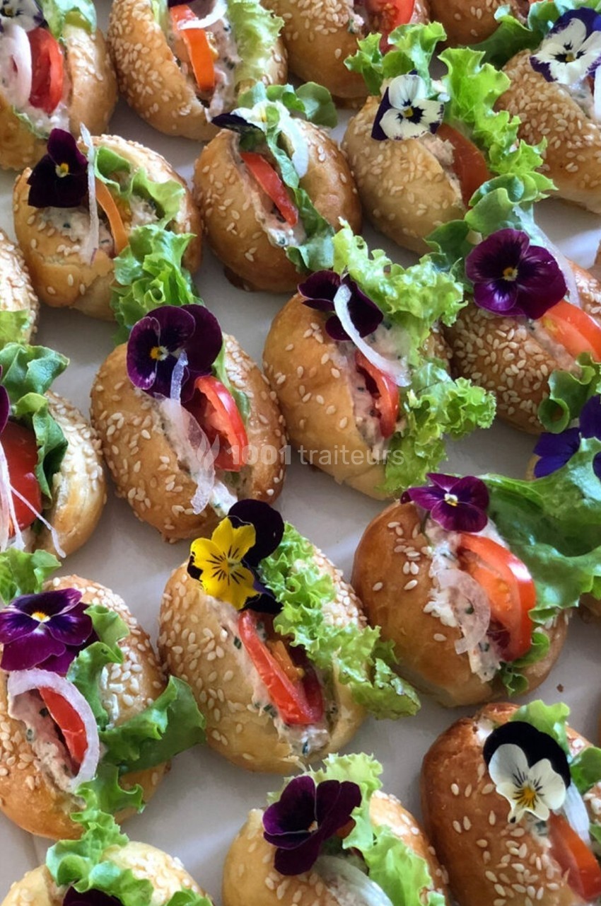 Mini-sandwiches garnis de salade, tomate, et fleurs comestibles sur pain aux graines de sésame.
