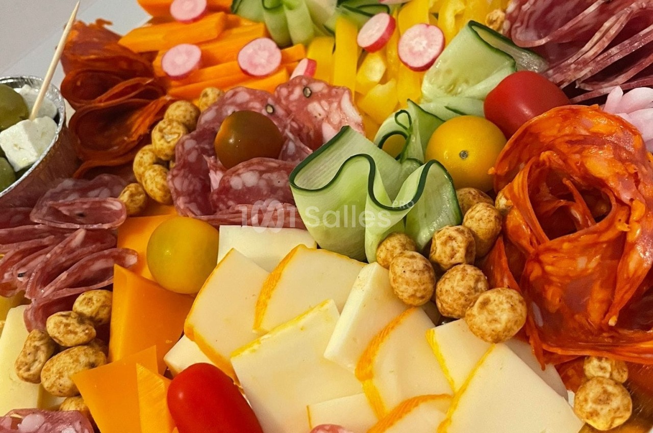 Plateau coloré de charcuteries, fromages, légumes frais, tomates cerises et olives, présenté pour un apéritif.