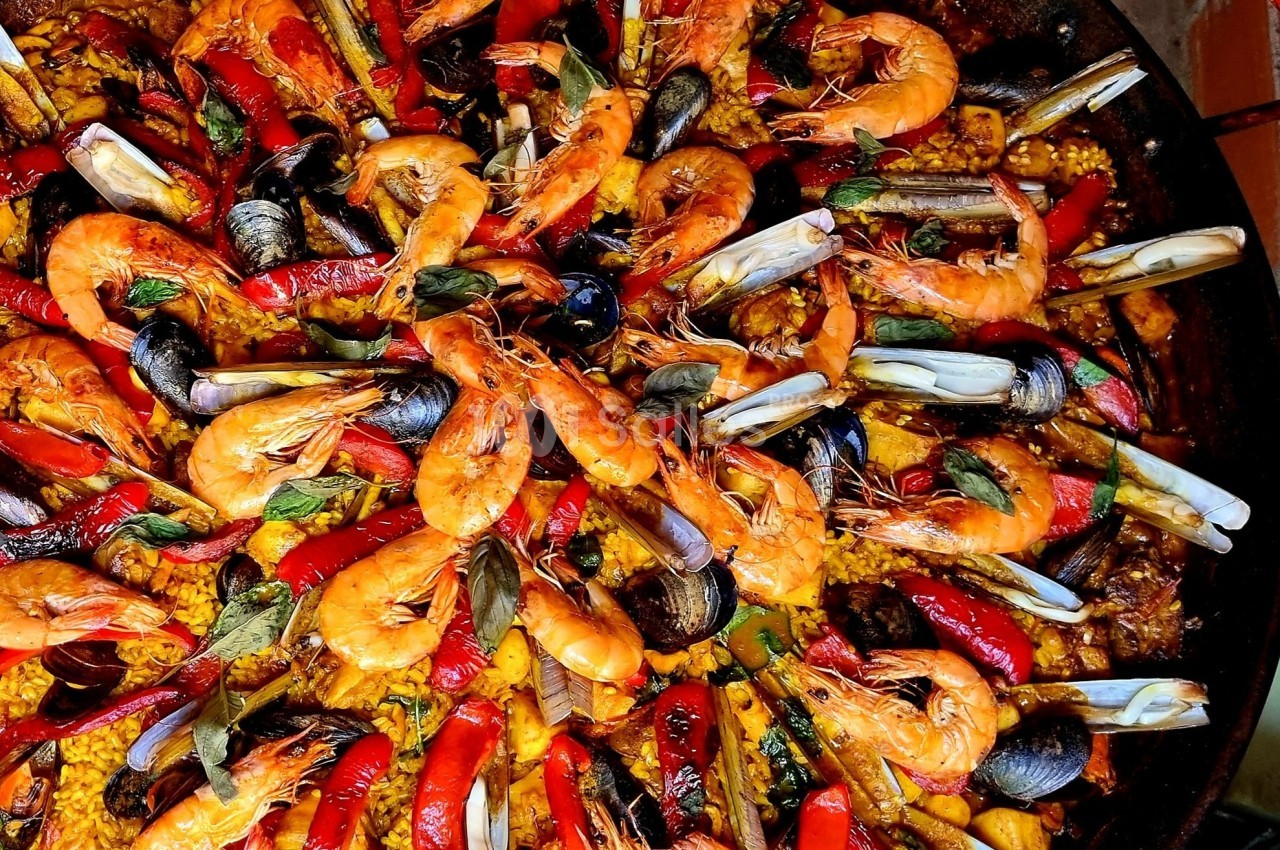 Plat de paella colorée avec crevettes, moules, poivrons rouges et riz safrané.